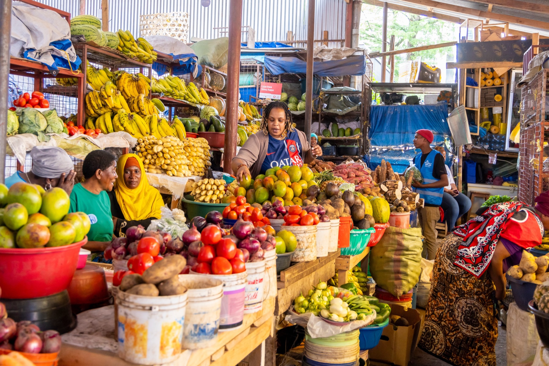 Vendors behind stacked displays of fruit and vegetables inside a covered market