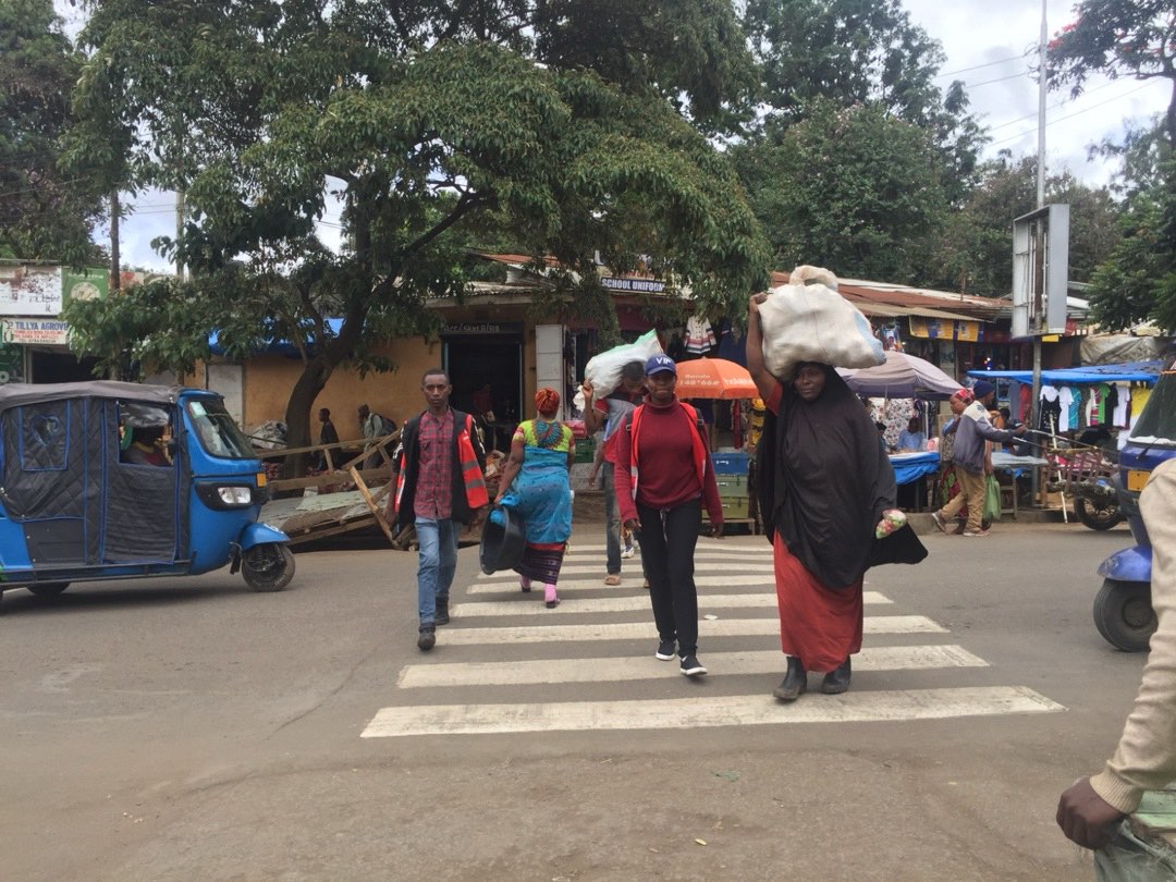 Shoppers crossing a market road on a zebra crossing, one carrying a sack on her head