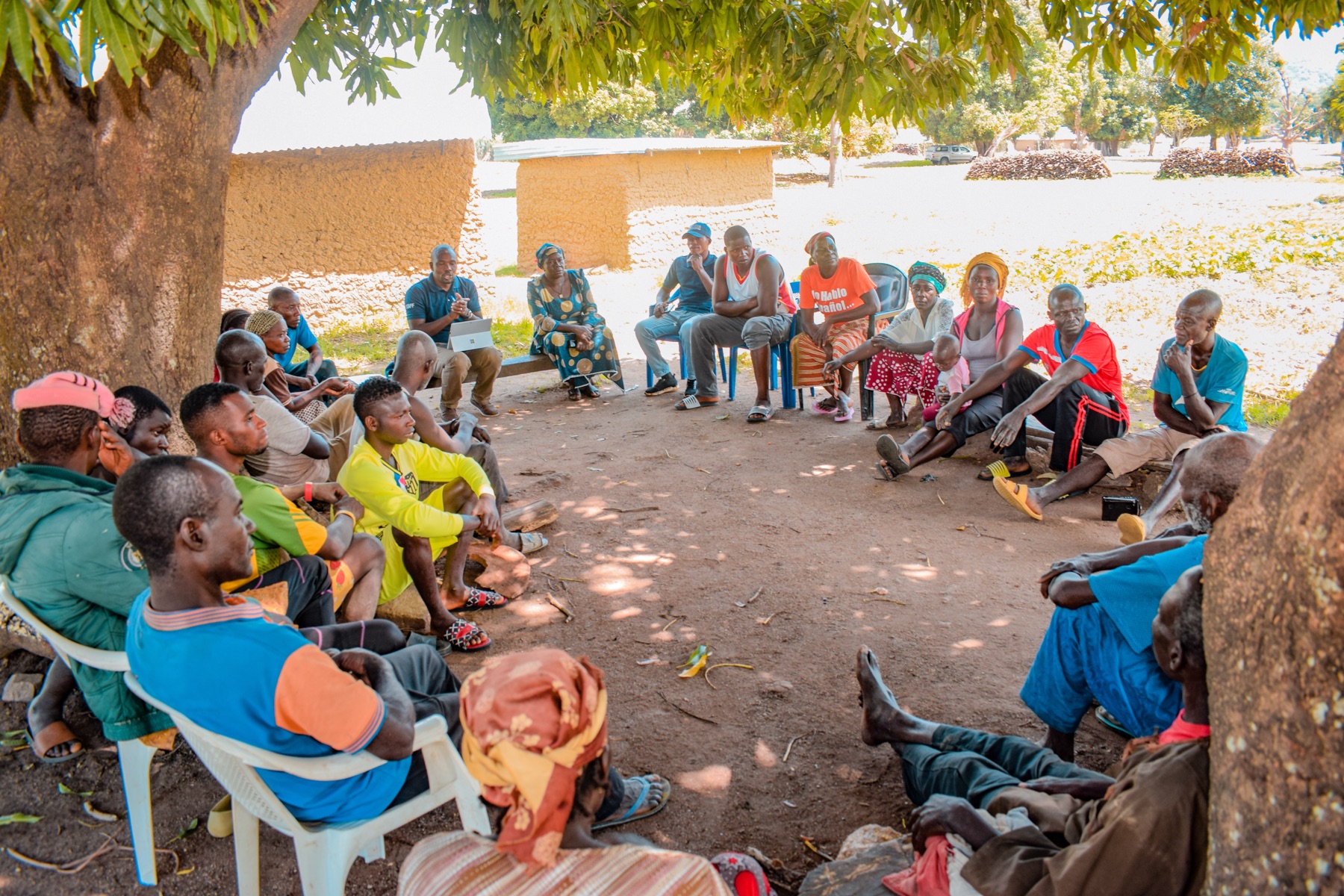 Members of a community group seated in a circle under a tree during a discussion